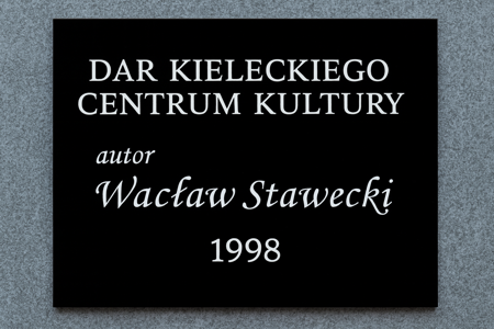 Tablica pamiątkowa z czarnej plexi z białym napisem: Dar Kieleckiego Centrum Kultury, autor Wacław Stawecki, 1998